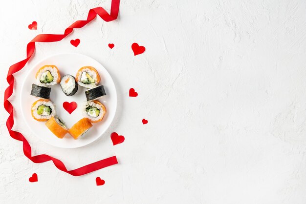 Rotoli di sushi per San Valentino con cuori rossi e nastro su un piatto bianco.