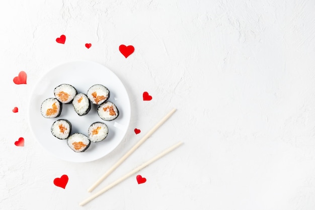 Rotoli di sushi per San Valentino con cuori rossi su un piatto bianco.