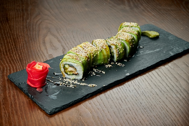 Rotoli di sushi vegani con cetriolo e avocado su una tavola di ardesia nera su un tavolo di legno. Cucina giapponese.