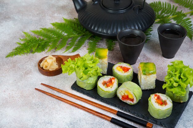 Rotoli di sushi vegetariano vegetale con una teiera di tè e tazze cinesi stanno su un tavolo di cemento.