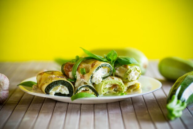 rotoli di zucchini cotti ripieni di formaggio all'interno di un piatto su uno sfondo verde