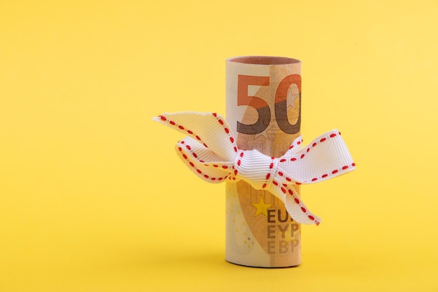 Rotolo di 50 euro di denaro con nastro bianco isolato su sfondo giallo concetto di regalo di denaro