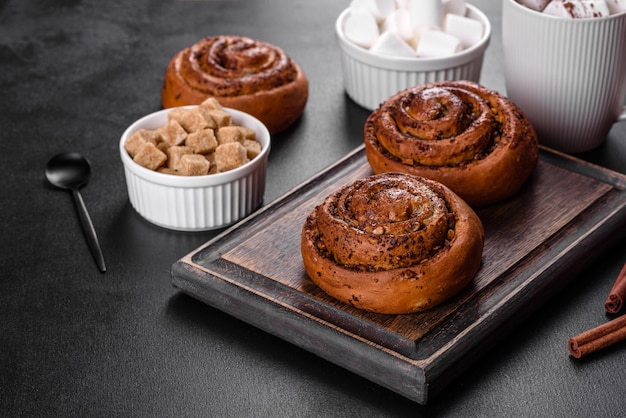 Rotolo di cannella appena sfornato con spezie e ripieno di cacao su sfondo nero. Panini alla cannella. Colazione svedese.