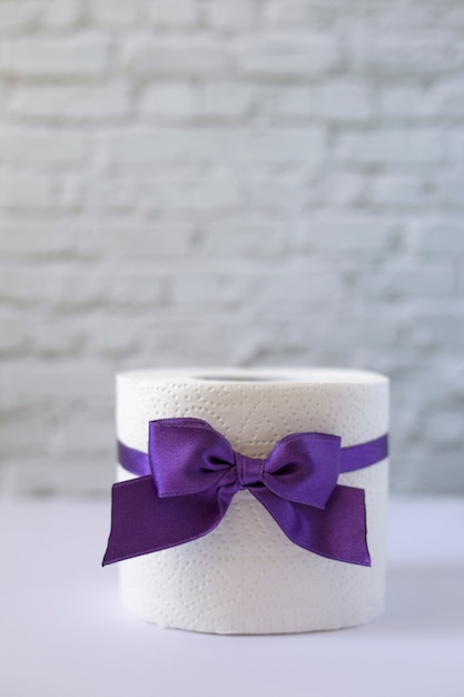 Rotolo di carta igienica bianca legata con nastro viola con fiocco, orientamento verticale. Rotolo di carta igienica con fiocco lilla
