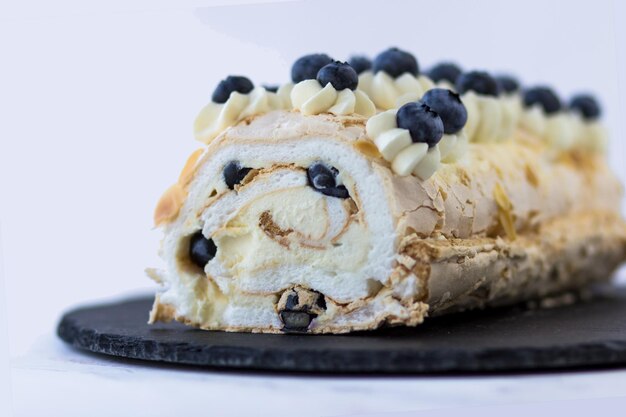 Rotolo di meringa con mirtilli su un piatto nero Dessert su sfondo bianco