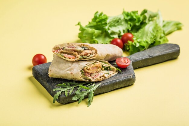 Rotolo di pane pita con un anello di gamberetti filettati, lattuga fresca e pomodorini su una tavola di legno su giallo