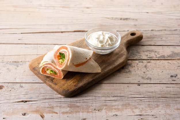 Rotolo di sandwich avvolgente di salmone con formaggio e verdure su tavola di legno