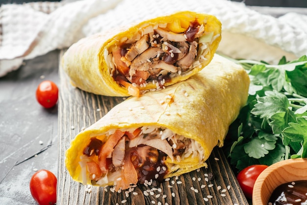 Rotolo di shawarma con semi di sesamo, salsa barbecue, pollo e verdure in pane pita su fondo di legno scuro con pomodorini e prezzemolo verde