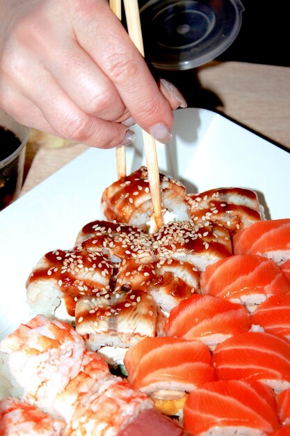 Rotolo di sushi con pesce fresco preso da una mano femminile con le bacchette