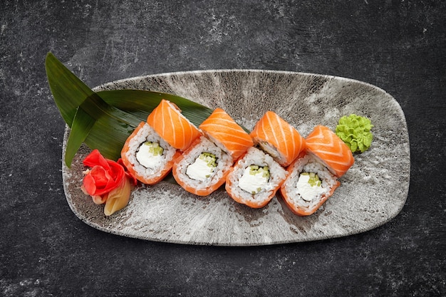 Rotolo di sushi della California con crema di formaggio e avocado al cetriolo e salmone su un piatto grigio su un tavolo scuro