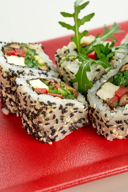 Rotolo di sushi di sesamo vegetariano vegetale in un piatto rosso su sfondo grigio