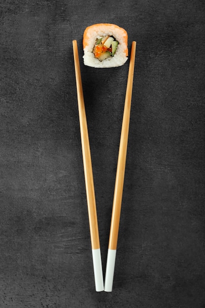 Rotolo di sushi e bacchette su sfondo scuro