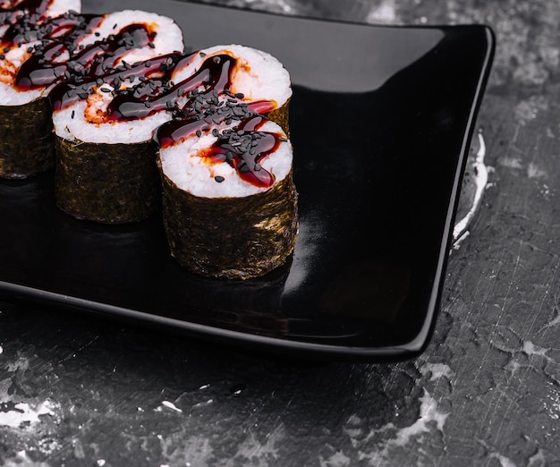 rotolo di sushi maki con anguilla e salsa unagi su un piatto nero
