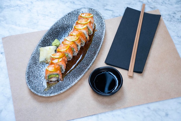 rotolo di sushi maki di salmone, avocado e gamberetti tagliati e bacchette inclinate dall'alto