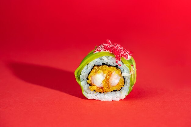 Rotolo di sushi singolo con avocado di gamberi e caviale di pesce volante su sfondo rosso Immagine creativa su sfondo a colori con ombra lunga