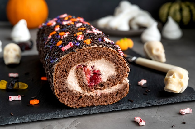 Rotolo di torta al cioccolato con panna e ciliegie decorate con caramelle di zucchero per halloween