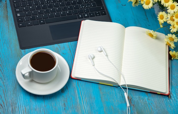 Roundup, cuffie per laptop, quaderno, caffè e fiori sul tavolo di legno blu