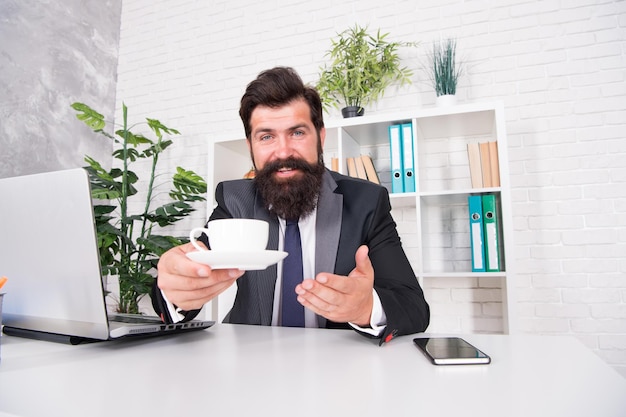 Routine della vita in ufficio Buongiorno Discuti di affari davanti a un caffè Rispettabile amministratore delegato Uomo bello capo seduto in ufficio a bere caffè Comodo spazio di lavoro Pantaloni a vita bassa barbuti Abito formale rilassante con caffè