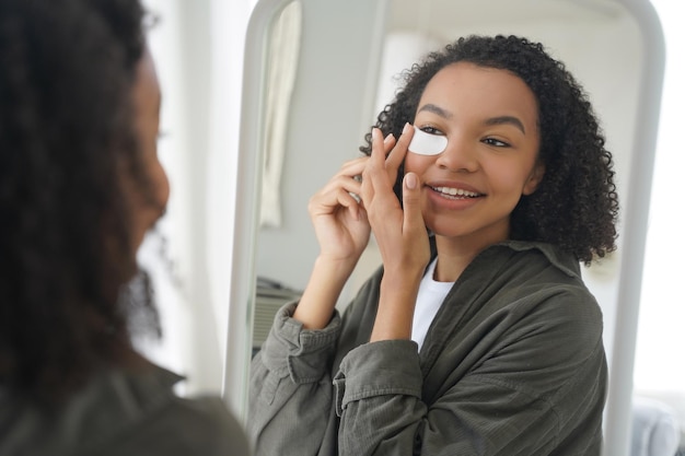 Routine di bellezza e cura della pelle mattutina Felice e attraente ragazza afroamericana sta applicando la benda sull'occhio