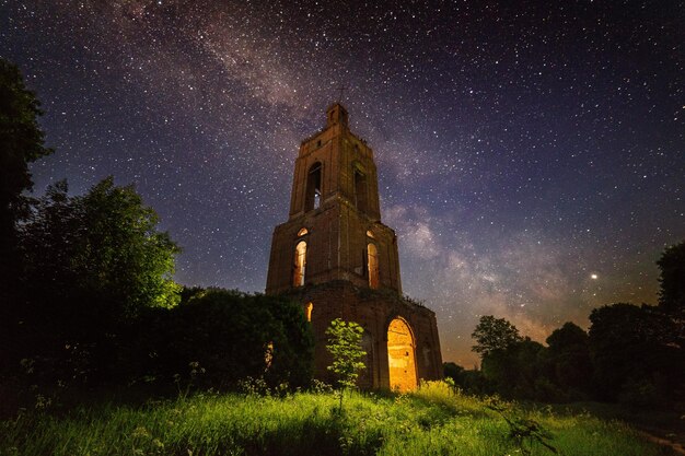Rovina del campanile notturno nella foresta di notte stellata con luce interna