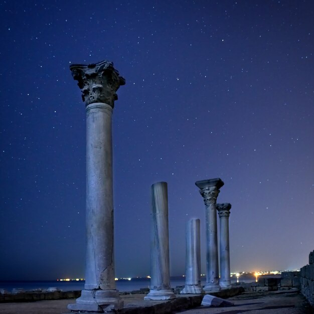 Rovine di antiche colonne della città sotto il cielo notturno blu con luna e stelle