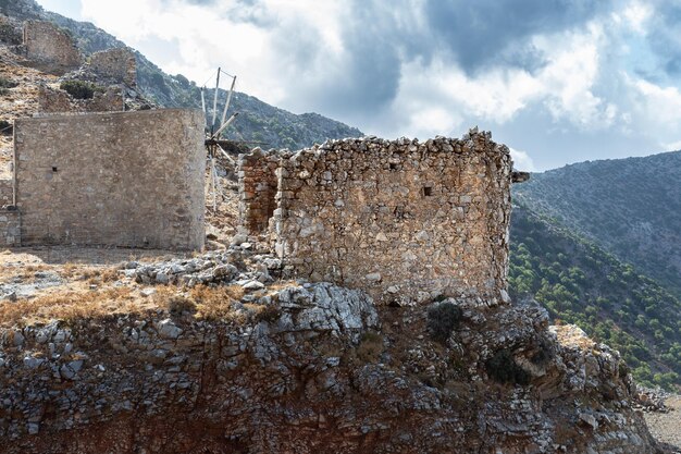 Rovine di antichi mulini a vento in pietra sulla scogliera con ripide montagne sullo sfondo al giorno Creta Grecia