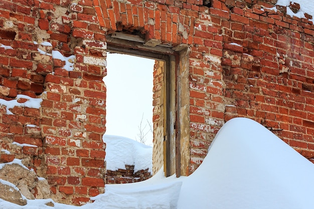 Rovine di un vecchio edificio con pareti in mattoni rossi con un foro per finestra e i resti di un telaio della finestra, coperto di neve