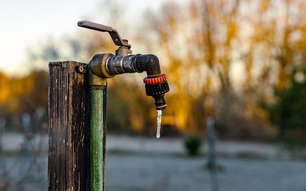 Rubinetto da giardino con goccia d'acqua congelata al mattino presto freddo