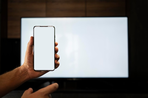 Rubinetto della mano dell'uomo adulto sullo smartphone con schermo bianco con tv a schermo bianco sullo sfondo nella notte Schermo bianco schermo vuoto Il modulo per il monitor delle informazioni senza informazioni e contenuto