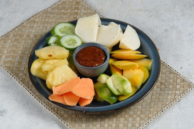 rujak buah o macedonia indonesiana su piatto bianco servito con salsa dolce piccante e arachidi macinate