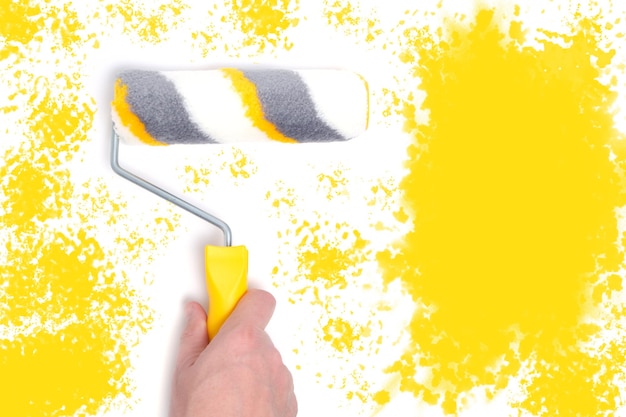 Rulli di vernice nelle mani per la pittura di pareti e riparazioni su sfondo giallo dipinto di bianco