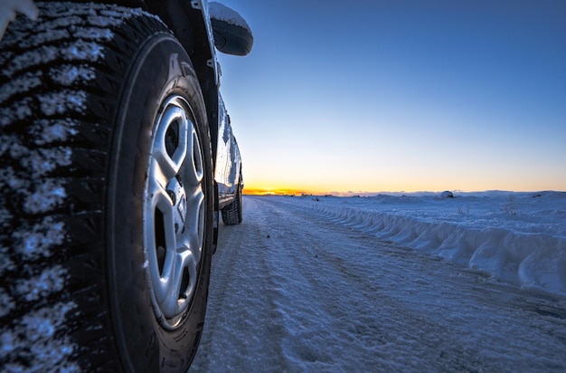 Ruota di auto 4x4 con ghiaccio su una strada completamente innevata con tracce di pneumatici che va all'orizzonte