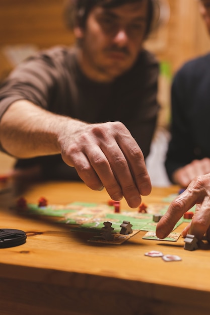 Russia, dicembre 2020: due amici uomini si divertono a giocare al gioco da tavolo carcassonne a tarda sera o di notte. mani maschili e carte da gioco e fiches sul tavolo