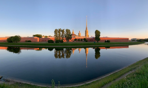 Russia, San Pietroburgo, il pittoresco riflesso della fortezza di Pietro e Paolo nel passaggio kronverksky su un tramonto, acqua calma, cielo blu, muro della fortezza di colore arancione