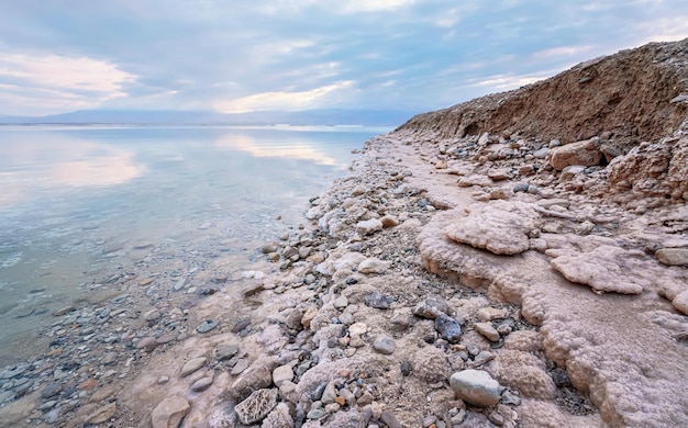 Sabbia e pietre ricoperte di sale cristallino sulla riva del Mar Morto, acqua limpida vicino - scenario tipico della spiaggia di Ein Bokek, Israele.