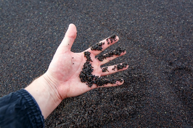 Sabbia nera vulcanica dalla spiaggia in mano maschile.