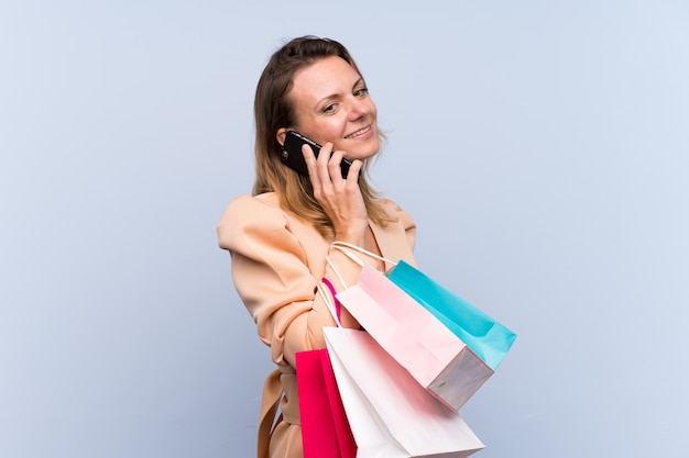 Sacchetti della spesa biondi della tenuta della donna e chiamare un amico con il suo telefono cellulare