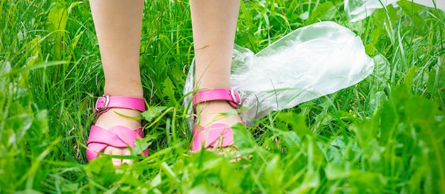 Sacchetti di plastica spazzatura con i piedi dei bambini sull'erba verde durante la pulizia del parco dai detriti di plastica