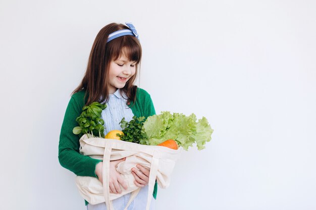 Sacchetto della spesa tessile della holding della bambina con le verdure. Rifiuti zero concetto. Acquisto di cibo senza pacchi. Borsa naturale ecologica con frutta e verdura biologica.