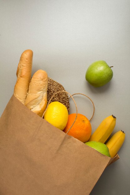 Sacchetto di carta con frutta e pane sulla superficie grigia