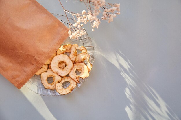 Sacchetto di carta con patatine di mela essiccate a fette spuntini sani sul piatto Vista dall'alto Una corretta alimentazione Concetto di cibo sano Decorazione floreale Gypsophila Foto di alta qualità