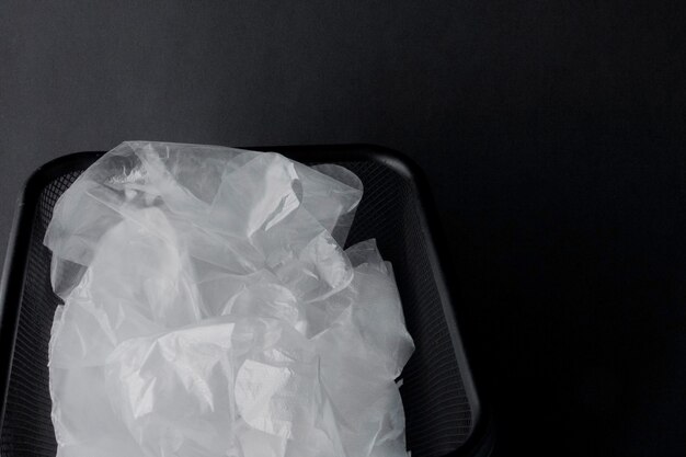 Sacchetto di plastica con manici, guanti nel cestino su sfondo nero. Sacchetto di plastica usato per il riciclaggio. Concetto - ecologia, inquinamento del pianeta con polietilene di cellophane di plastica.