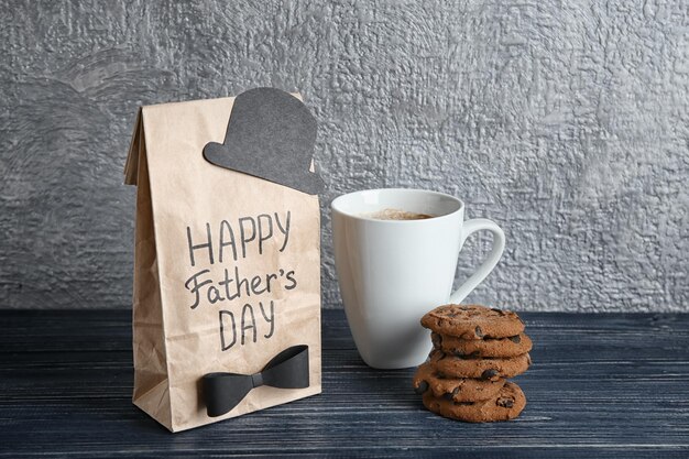 Sacco di carta con testo BUONA FESTA DEL PADRE tazza e biscotti sul tavolo