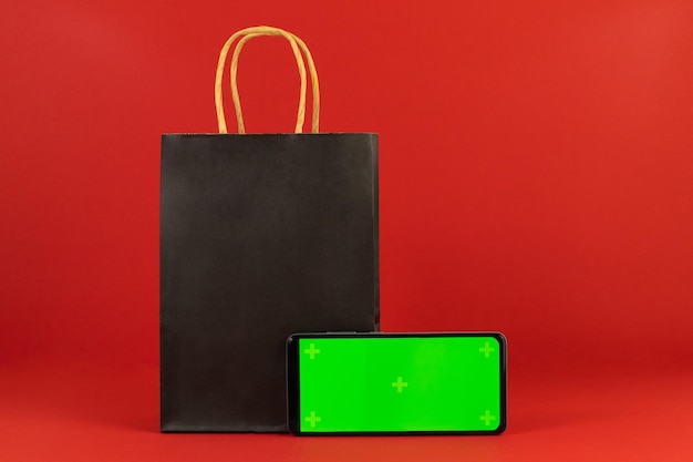 Sacco di carta nero e telefono con schermo verde su sfondo rosso. Venerdì nero, vendita, promozione, shopping,