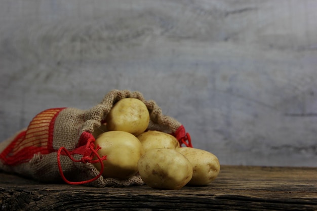 Sacco di iuta di patate novelle da fattoria ecologica su fondo di legno