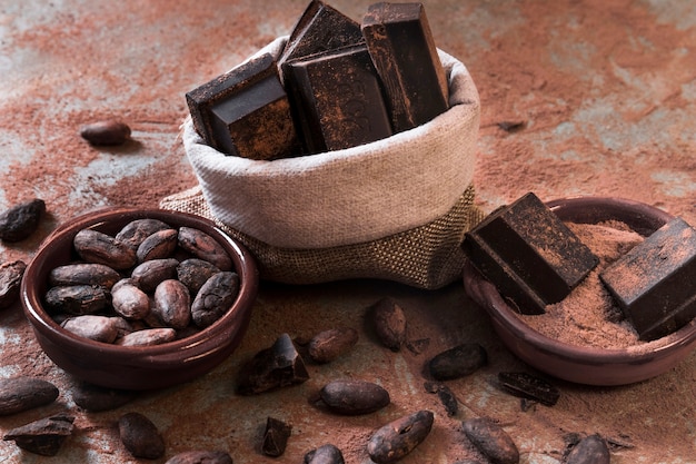 Sacco di pezzi di barretta di cioccolato e polvere di cacao e fagioli sul ripiano del tavolo