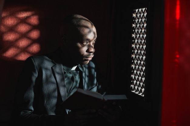 Sacerdote africano che legge la Bibbia seduto in confessionale