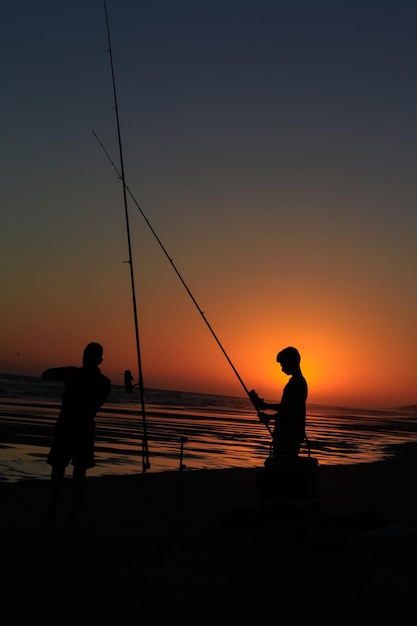 sagoma di due giovani pescatori su una spiaggia al tramonto