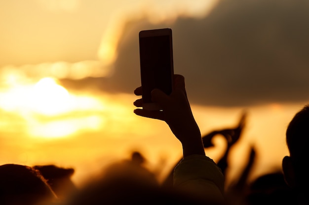 Sagoma di mani che utilizzano smartphone per scattare foto e video in uno spettacolo di musica dal vivo.