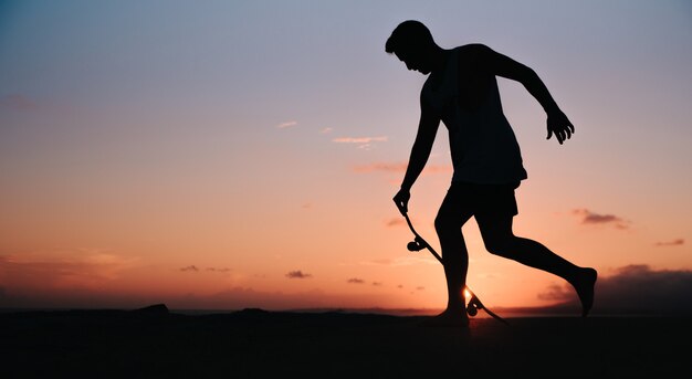 Sagoma di un giovane ragazzo a piedi nudi cavalcando uno skateboard al tramonto